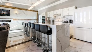 A modern kitchen with white cabinets, a marble countertop, and a bar area with stools.