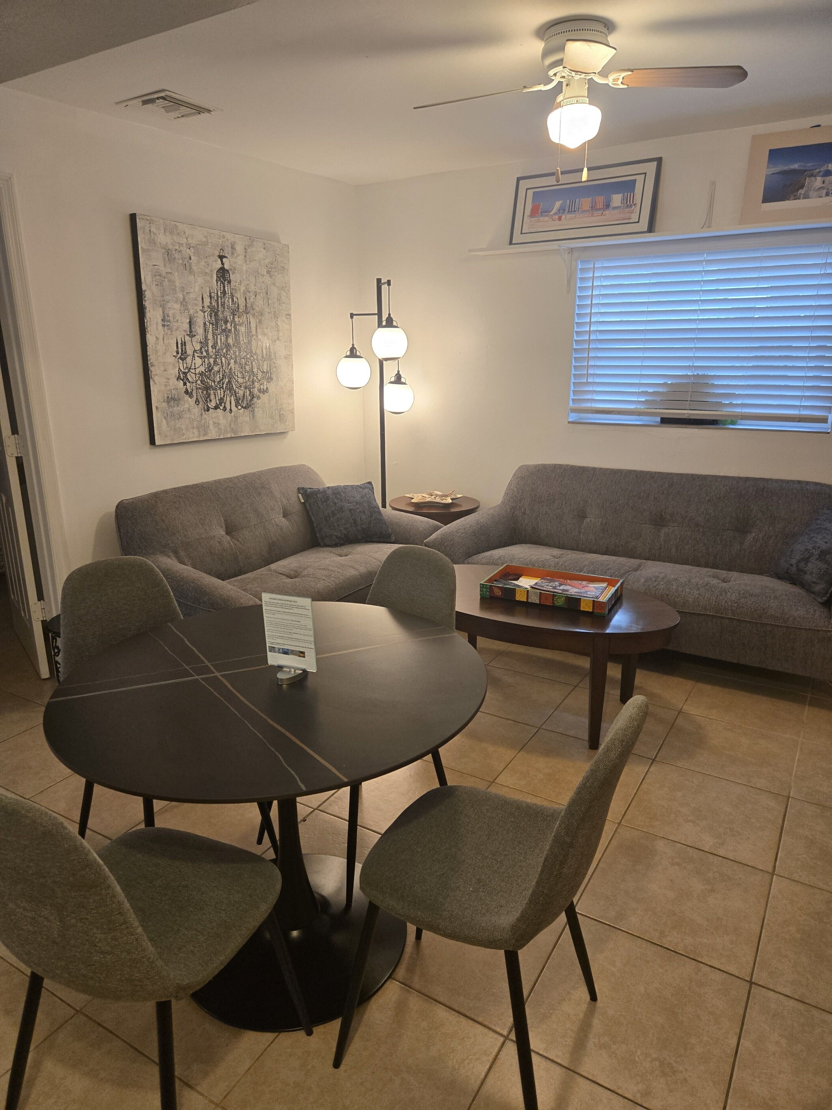 A living room with a dining table, two sofas, a floor lamp, and a ceiling fan.