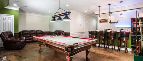 A billiards room with a pool table, leather chairs, and a billiard table.