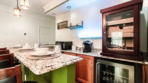 A kitchen with a granite countertop, green cabinets, a wine cooler, and a billiard cue rack.