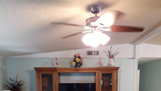 A living room with a TV, wooden cabinet, sofas, and a ceiling fan. - Clean spacious 2BR mobile home in great senior community in Largo Florida (Largo)