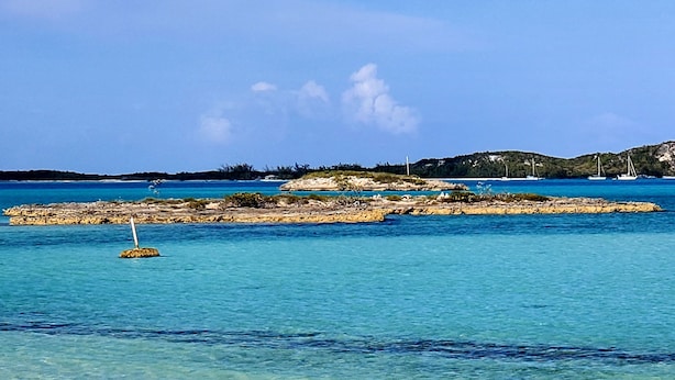 Una platja amb aigua turquesa cristal·lina, sorra daurada i roques al fons.