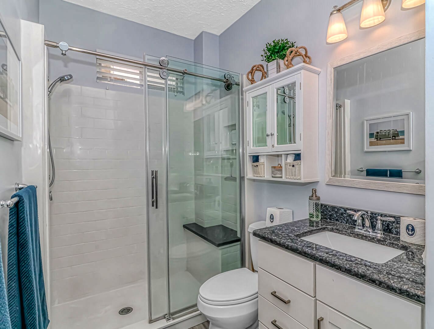 A modern bathroom with a glass-enclosed shower, white cabinetry, a marble sink, and a large mirror.