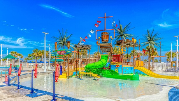 Ein Wasserpark mit einer großen, grünen Wasserrutsche, einem Poolbereich und Palmen.