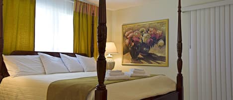 A four-poster bed with a canopy, a painting of flowers on the wall, and a ceiling fan.
