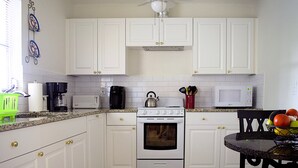 Een keuken met witte kastjes, een fornuis, een magnetron en een eethoek met een tafel en stoelen.