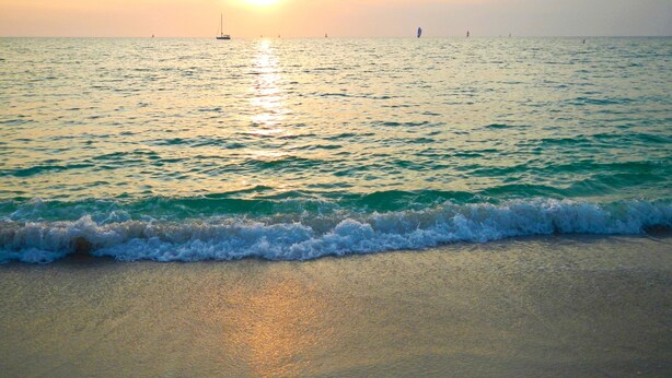 Een strand met golven en een ondergaande zon op de achtergrond.