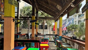 A colorful outdoor seating area with tables and chairs, a covered section with a mesh roof, and a view of buildings in the background. - Updated villa minutes walk to the beach. Seasonal heated outdoor pool (Hilton Head Island)