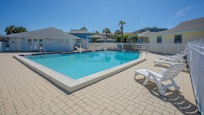 En rektangulär swimmingpool med en kakelbeklädd poolkant, omgiven av vita solstolar och ett vitt staket.