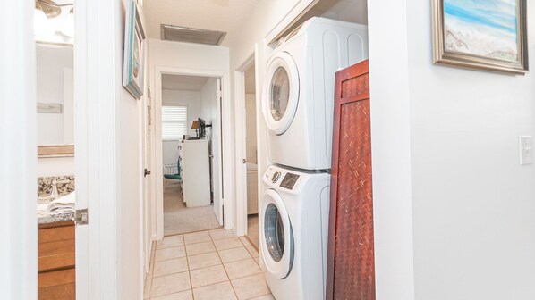 Un lavadero con dos lavadoras y secadoras apiladas, un escritorio pequeño con una computadora, y una puerta que da a otra habitación.
