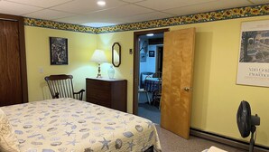 A hotel room with a bed, a chair, a dresser, a mirror, and a door leading to another room.