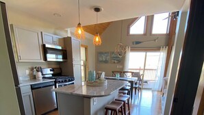 A modern kitchen with a central island, wooden flooring, and pendant lighting.