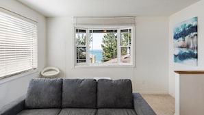A modern living room with a gray sofa, a bay window with a view of the sea, and a minimalist white side table.