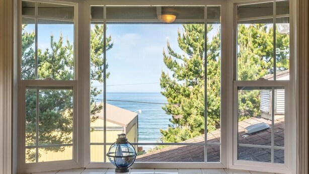 A bay window with a clear view of the ocean and surrounding trees.