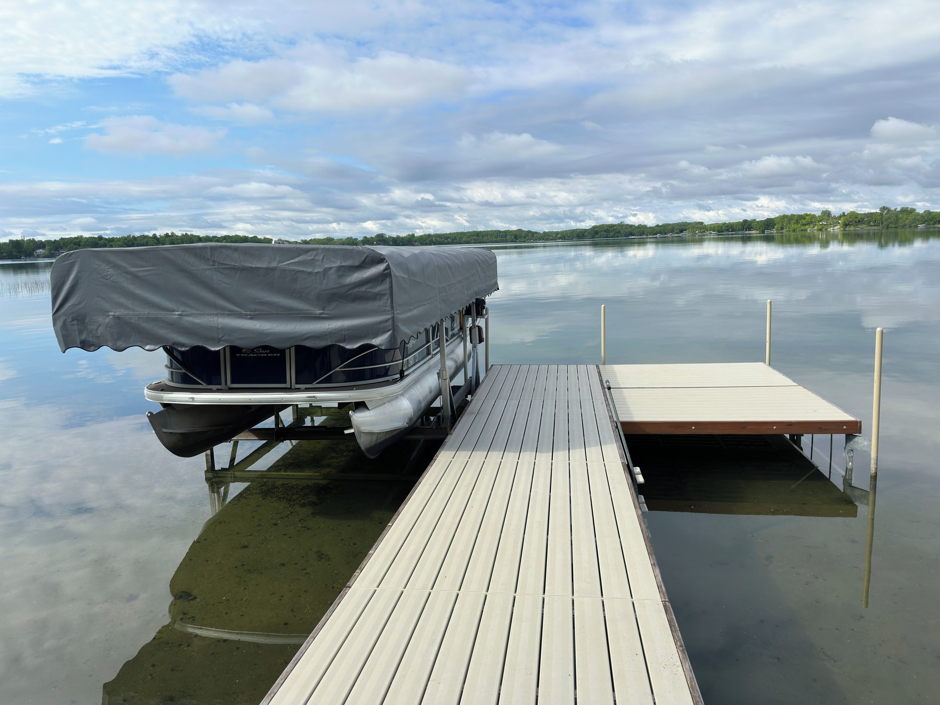 A boat with a canopy on a wooden dock extending into a calm lake.