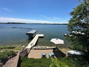 Une jetée au bord du lac, avec un abri pour véhicules, un bateau et une zone de plage équipée de chaises longues et d’un parasol.