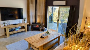 A cozy living room with a flat-screen TV, a wooden coffee table, a fireplace, and a sliding glass door leading to an outdoor area. - Abercrombie Ridge - Lux LODGE and Spa Retreat - Pet-friendly (Curraweela)