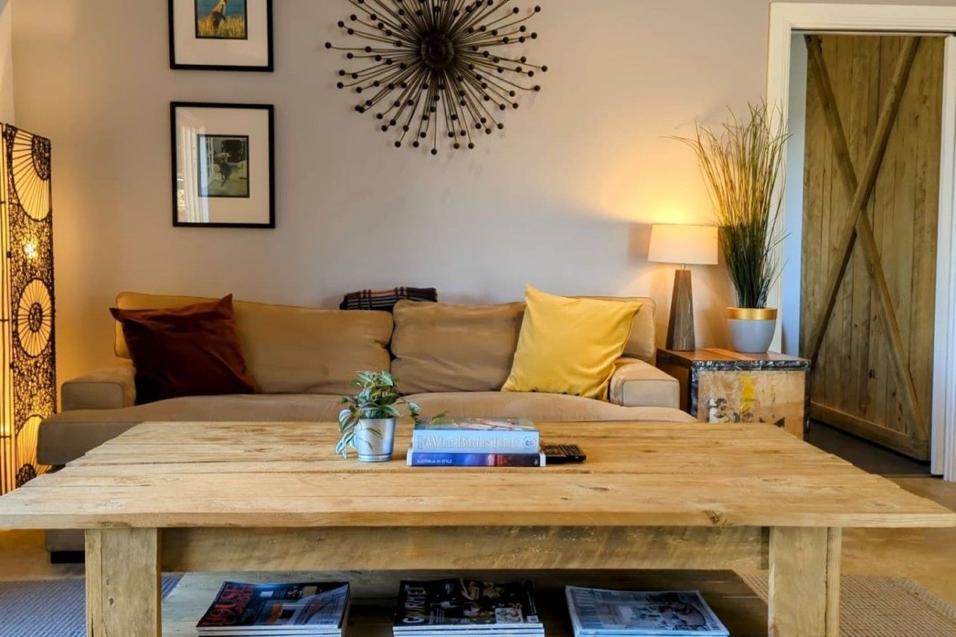 A living room with a sofa, a coffee table, a wall clock, and a door with a wooden shutter.