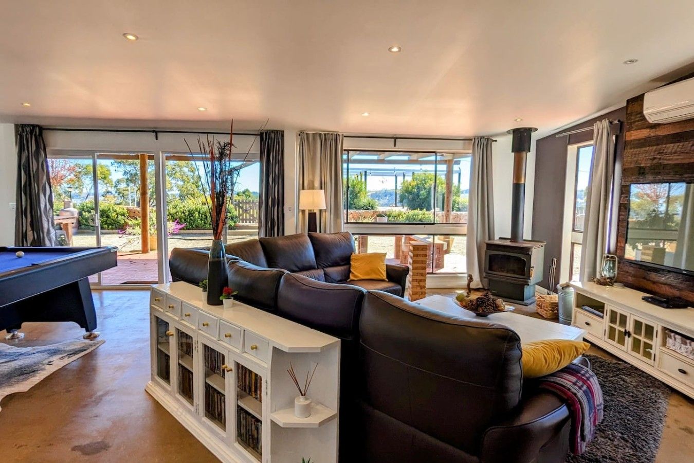 A spacious living room with a pool table, comfortable seating, a fireplace, and a television.