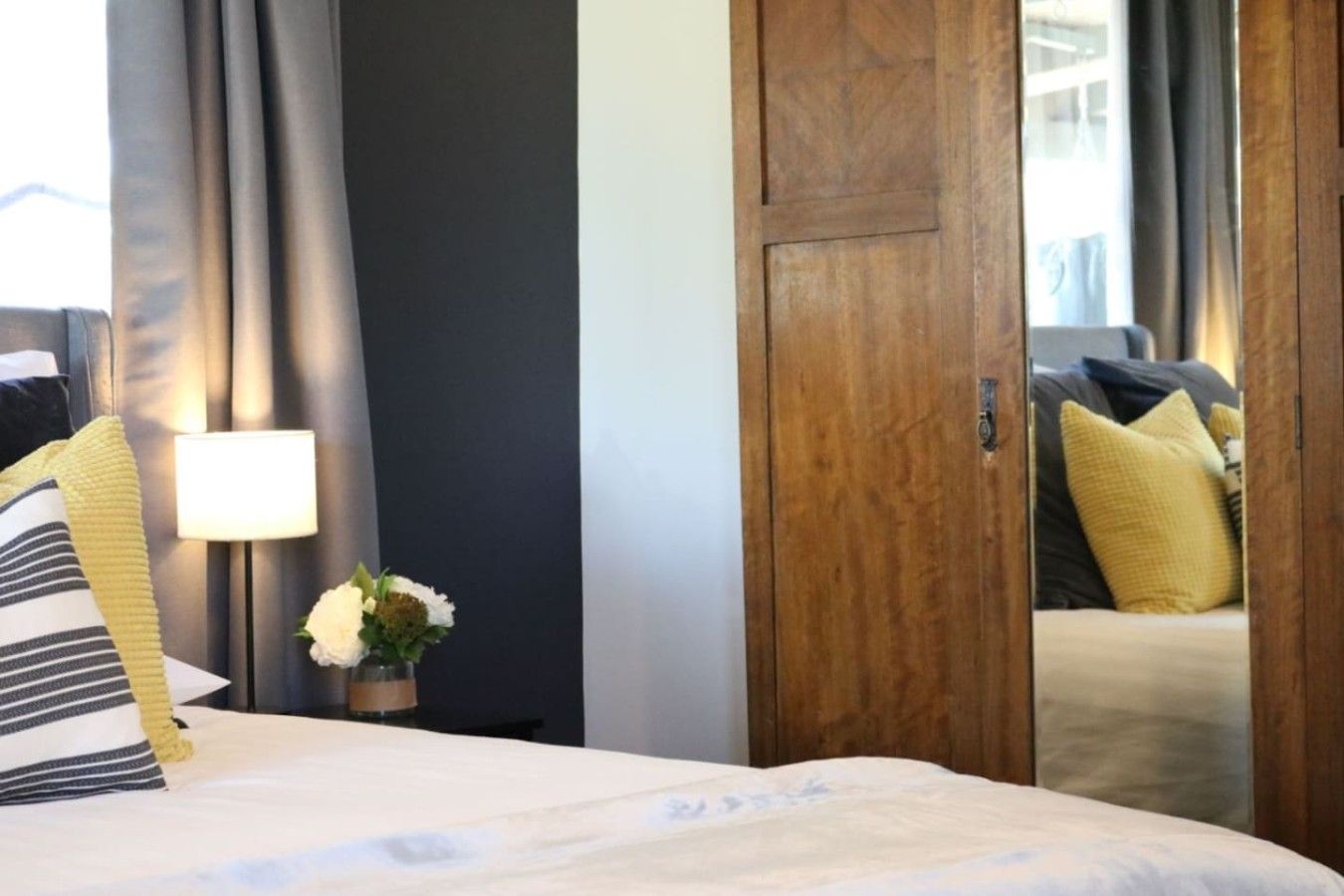 A hotel room with a bed, a nightstand, a lamp, a flower arrangement, and a wooden door.