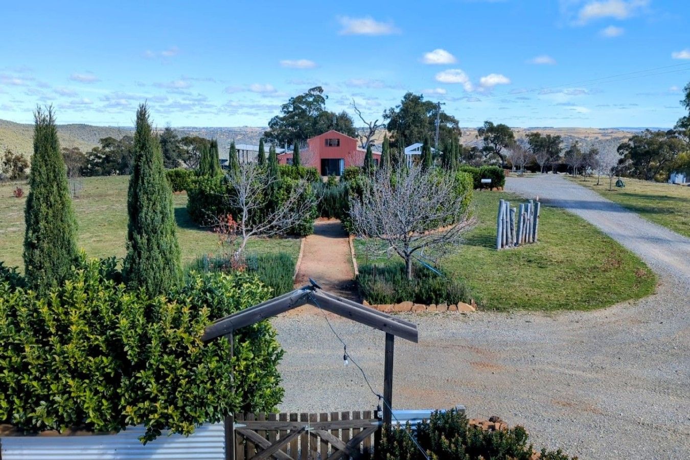 A residential property with a paved driveway leading to a red building, surrounded by well-maintained lawns and trees.
