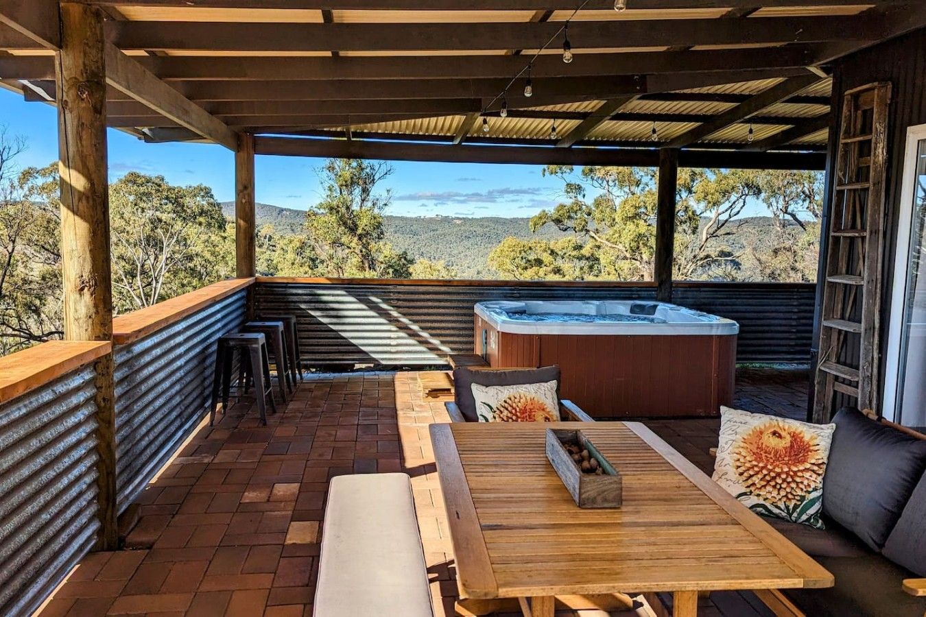 An outdoor patio with a wooden table, benches, and a hot tub.