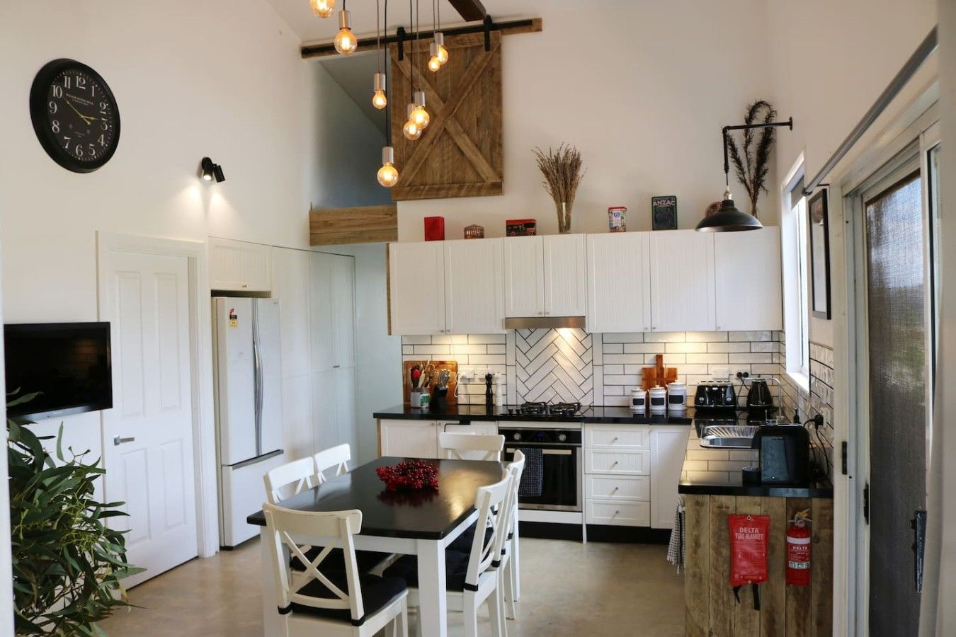 A modern kitchen with white cabinets, a black countertop, a dining table with chairs, and a wall-mounted clock.