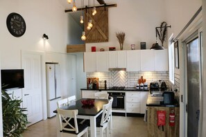 A modern kitchen with white cabinets, a black countertop, a dining table with chairs, and a wall-mounted clock. - Abercrombie Ridge - Lux LODGE and Spa Retreat (Curraweela)