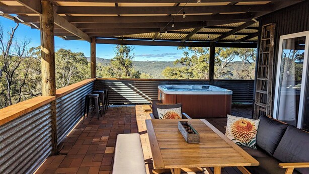 A covered patio with a hot tub, wooden furniture, and a view of the surrounding landscape. - Abercrombie Ridge - Lux LODGE and Spa Retreat - Pet-friendly (Curraweela)