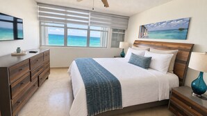A bedroom with a bed, a nightstand, a dresser, a ceiling fan, and a window with a view of the ocean. - Beachfront in * Isla Verde * walk 2 eat * (Carolina)