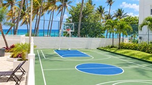 An outdoor basketball court with a view of the ocean, surrounded by palm trees and a fence. - Beachfront in * Isla Verde * walk 2 eat * (Carolina)