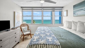Une chambre à coucher avec un lit, une chaise, un téléviseur, un ventilateur de plafond et une vue sur l’océan.