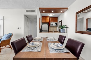 Un comedor con una mesa de madera, cuatro sillas y una cocina visible a través de una puerta abierta.