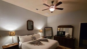 A bedroom with a bed, bedside tables, a ceiling fan, a TV, and a mirror.