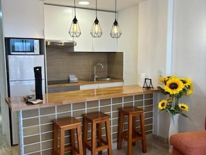 Une cuisine moderne dotée d’un plan de travail en bois, de deux tabourets de bar, d’un four à micro-ondes encastré et de luminaires suspendus.