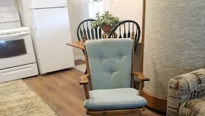 A kitchen with white appliances, a wooden dining table, a blue upholstered chair, and a brown leather ottoman. - Bungalo off the Withlacooche (Dunnellon)