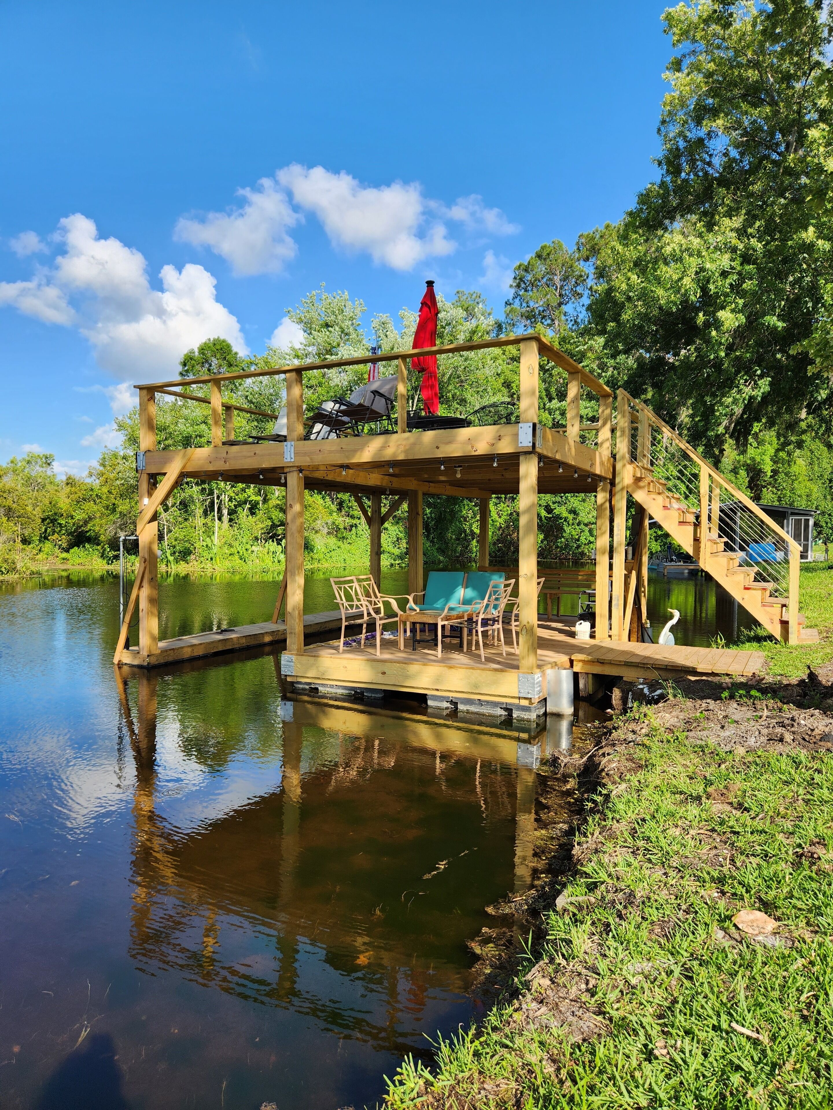 A wooden deck with chairs and an umbrella, overlooking a calm body of water.