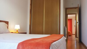 Ein Hotelzimmer mit einem Bett, einem Nachttisch mit Lampe, einem Holzschrank und einer Tür zu einem weiteren Raum.