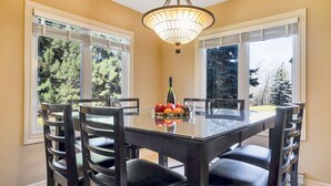 A dining area with a glass table, black chairs, a chandelier, and a window with blinds.