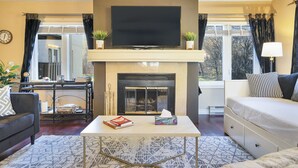 A living room with a fireplace, a sofa, a coffee table, and a TV mounted above the fireplace.