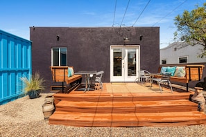 Relax in a sheltered outdoor space with a metal table, chairs, and a wooden bench, surrounded by lush greenery.