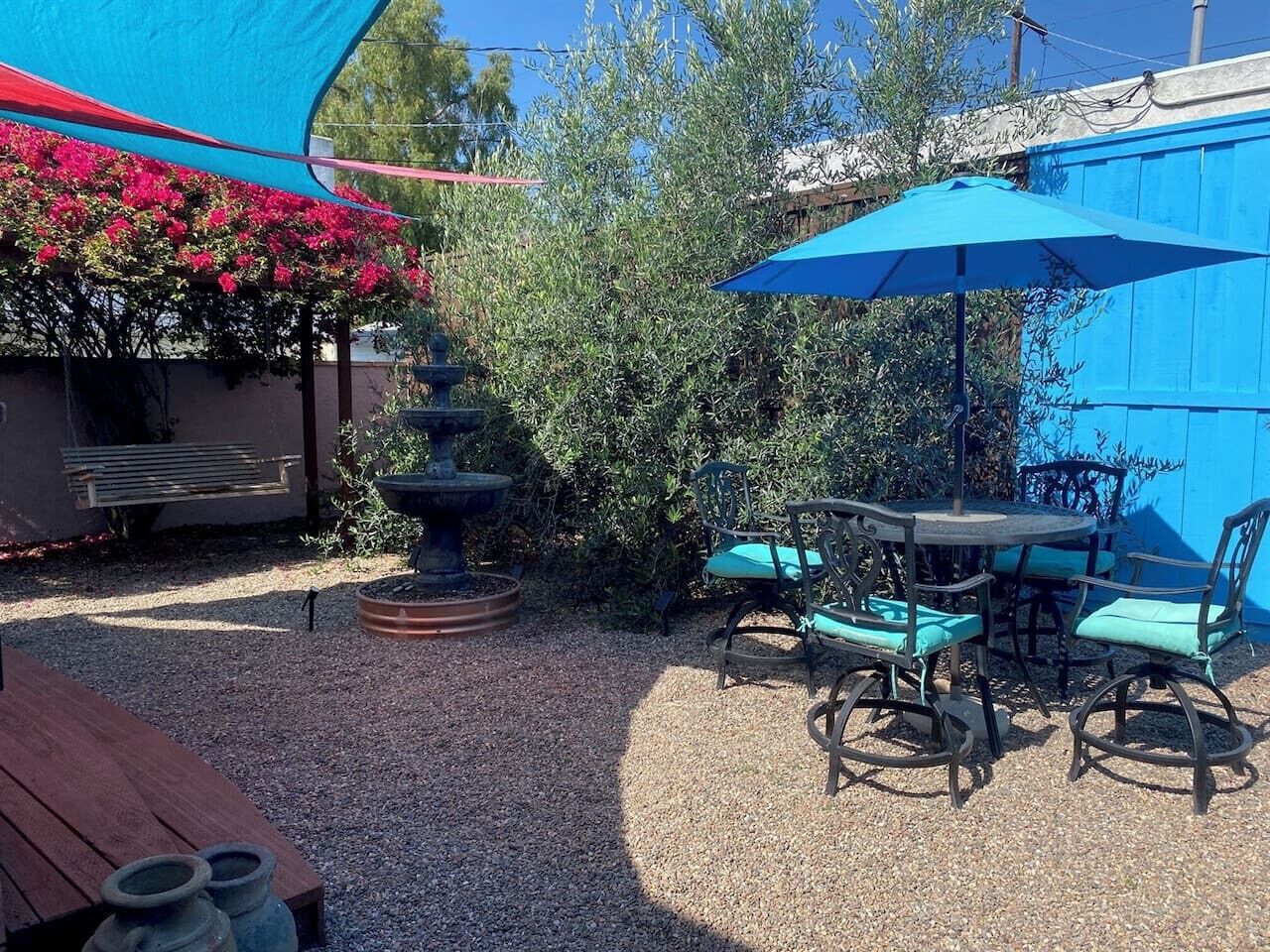 Un espace patio avec une table ronde et des chaises, un parasol bleu et une fontaine.