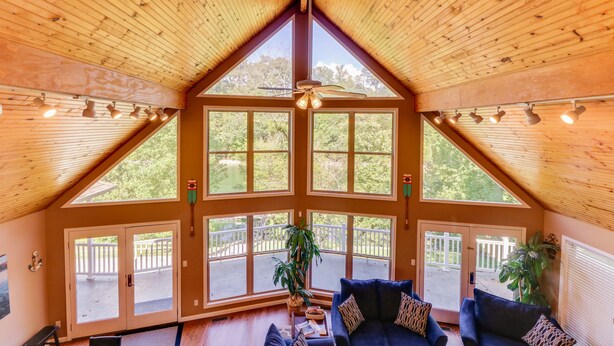 A spacious room with a high ceiling, large windows, and a ceiling fan. - Lakehouse with covered dock, slide, and outdoor kitchen! Close to I-75, trails. (Caryville)