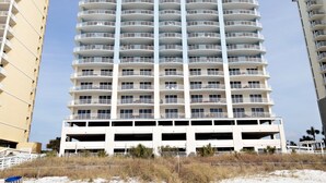 A high-rise hotel with multiple balconies, a parking garage, and a sandy beach in the foreground. - OPEN 10/3-10/5 OR 10/19-10/26 2 FREE Beach chairs  Condo on the Beach (Panama City Beach)