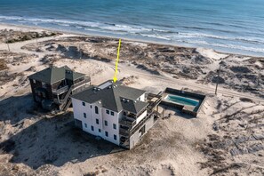 An aerial view of a beachfront property with multiple buildings, a swimming pool, and a sandy beach area.