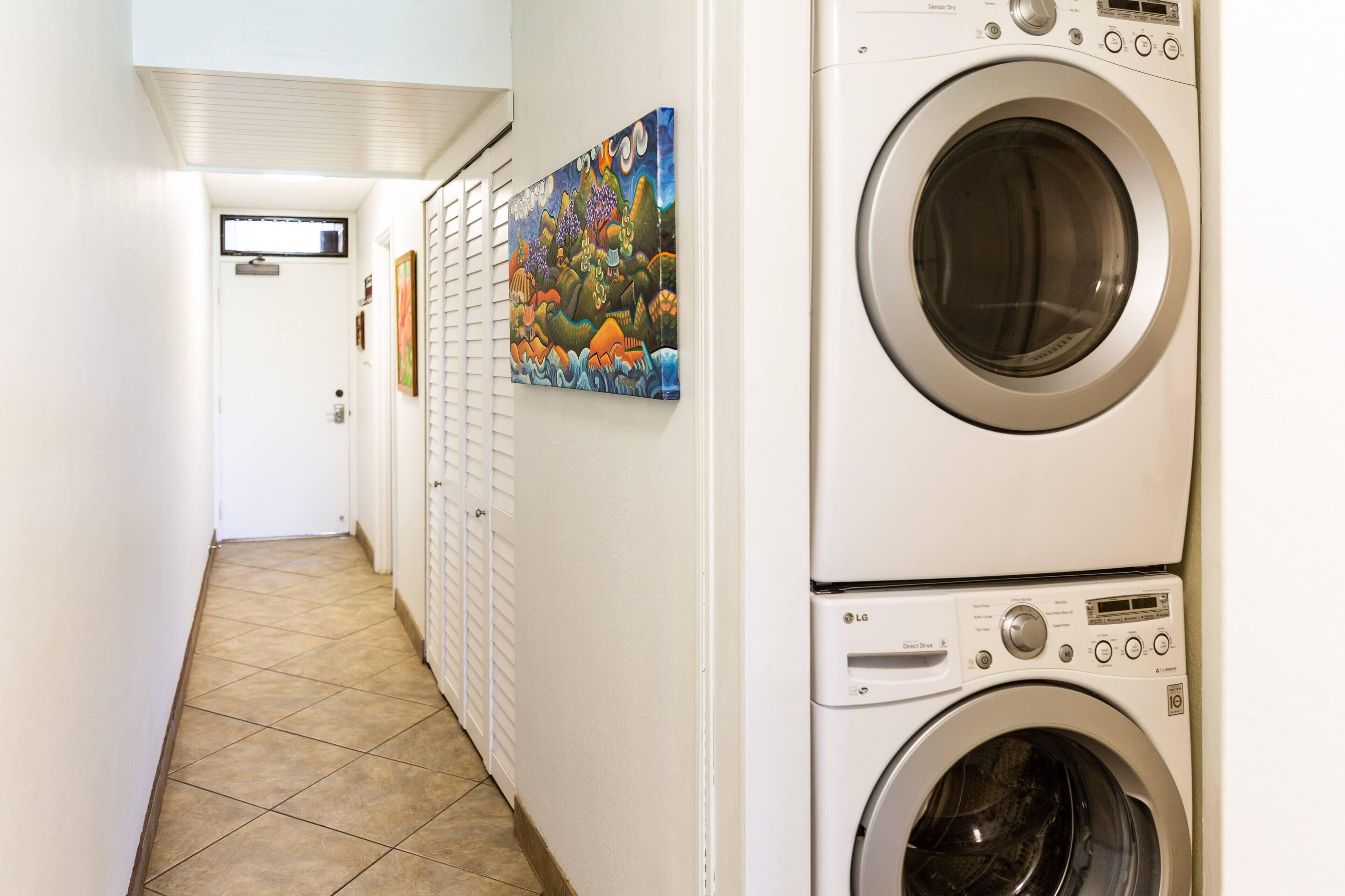 A laundry room with two stacked front-loading washing machines, a tiled floor, and a colorful mural on the wall.