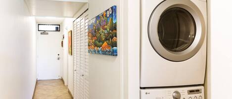 A laundry room with two stacked front-loading washing machines, a tiled floor, and a colorful mural on the wall.