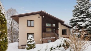 Ein zweistöckiges Haus mit verschneiter Fassade, einer Veranda und einem kleinen Vorgarten mit einem schneebedeckten Baum.