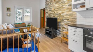 Ein modernes Wohnzimmer mit Fernseher, Holzboden, Steinwand und Küchenzeile mit Schränken und Backofen.