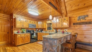 Une cuisine rustique dans une cabane en bois, avec un îlot central en pierre, des armoires en bois et une décoration représentant un ours sur le mur.
